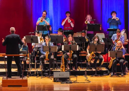brass and sax players with music stands on tiered seating